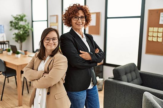 Zwei Erwachsene Frauen arbeiten zusammen im Büro: eine mit und eine ohne Behinderung.